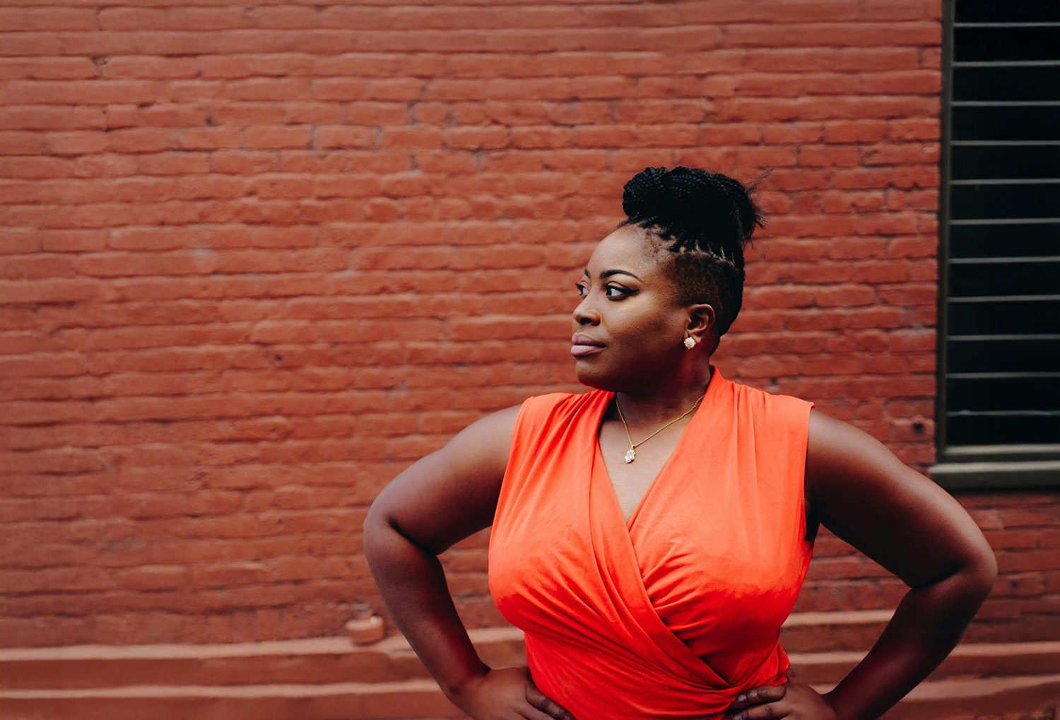 Photograph of a young Black woman standing in front of a red brick wall outdoors. She looks off to the side with a pensive but warm expression. This image represents a new homeowner navigating property tax issues and is not an actual photo of the individual in the case story.