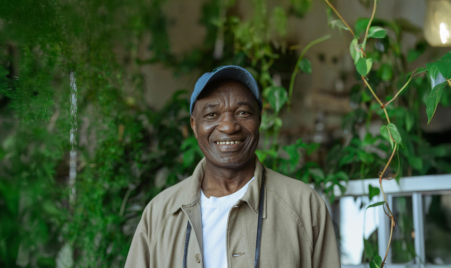 A portrait-style photograph of an older man wearing a blue baseball cap, looking directly at the camera and smiling. He is outdoors in soft, contemplative lighting, symbolizing a tenant’s experience navigating complaint processes.
