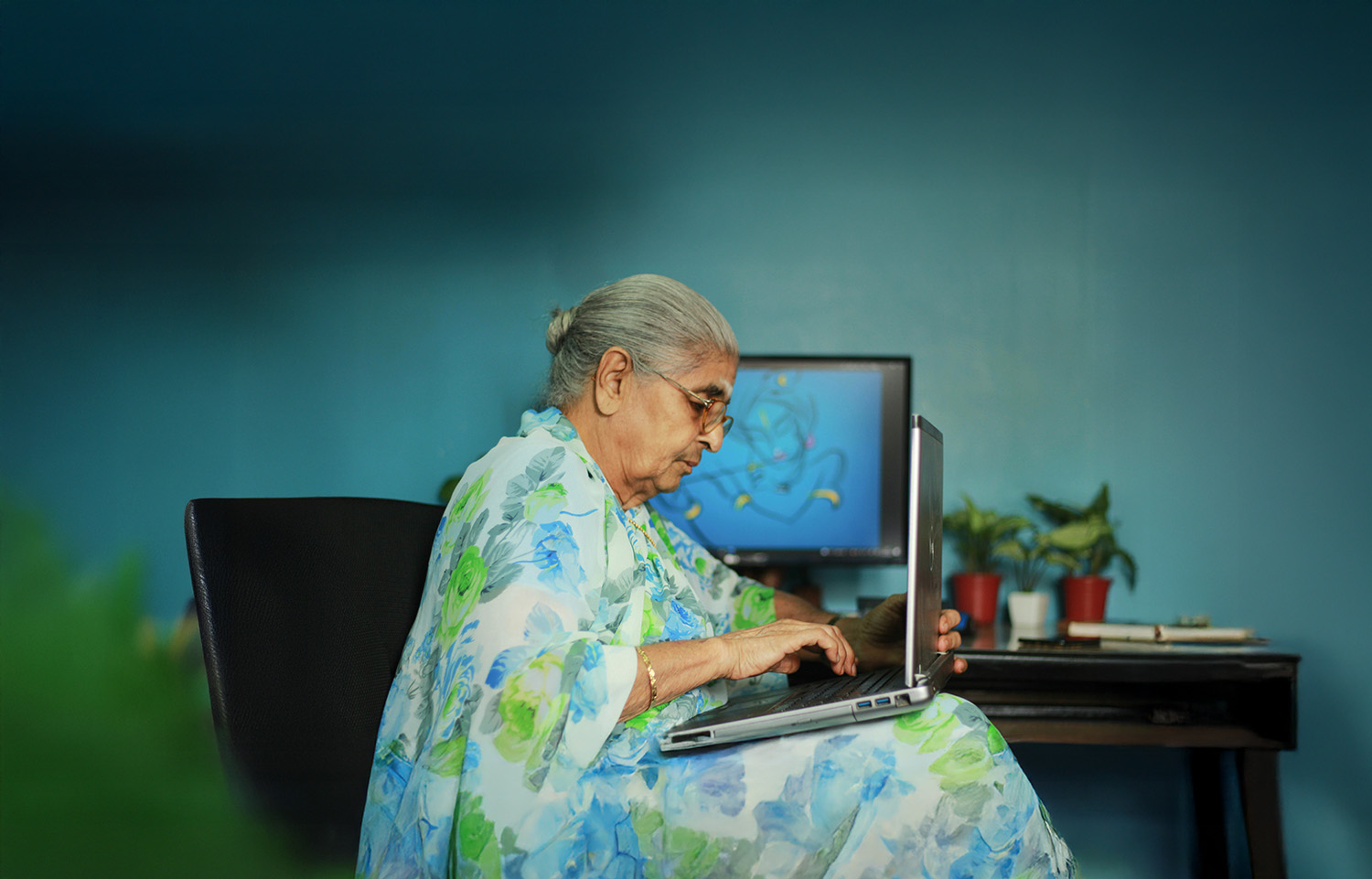 A documentary-style photo of a senior woman with gray hair and glasses, seated in a softly lit room and using a computer. She is focused, looking down at the screen. The image is intended to represent a tenant facing eviction and is not an actual photo of the individual in the case story.