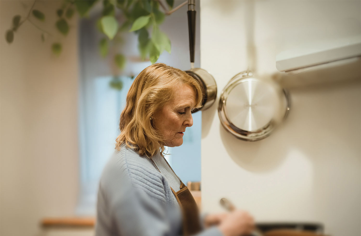 A middle-aged woman is photographed in a documentary style in her kitchen. She looks down at a pot she is stirring. This image portrays everyday life for Torontonians supported by Ombudsman Toronto.
