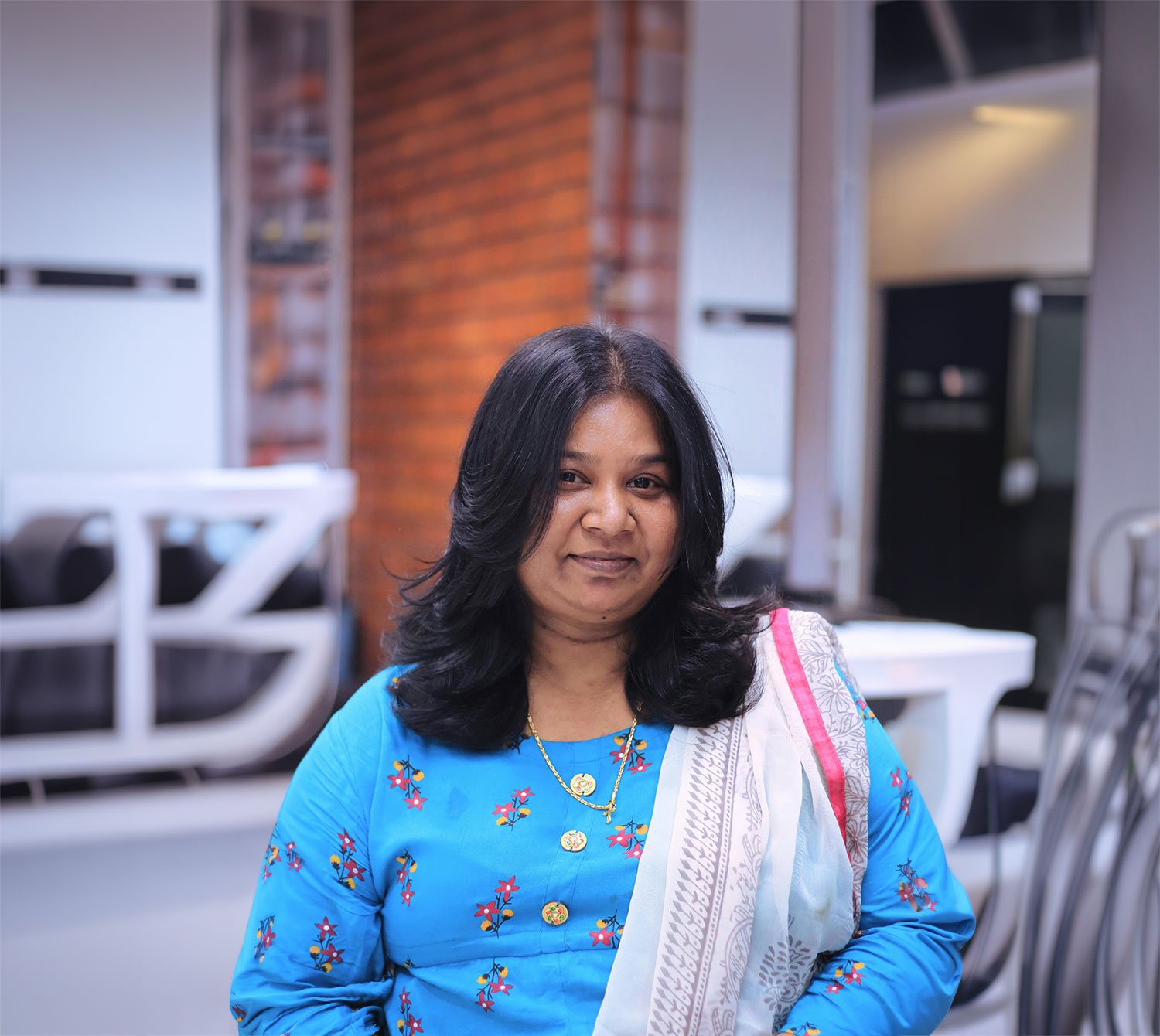 A South Asian woman looks directly at the camera with a warm gaze and soft smile. The blurred background suggests an outdoor setting. She represents Shabina, the person in the case story.
