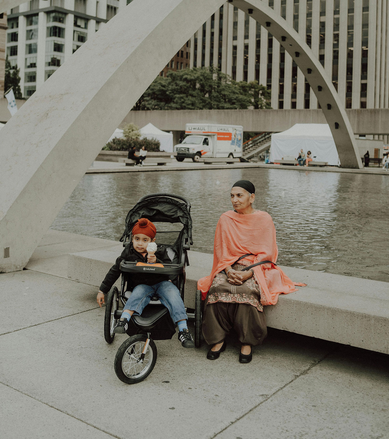 A senior woman with a headscarf and a pink shawl sits pensively with her grandson in a stroller. She looks away from the camera, lost in thought. The image represents the senior complainant in the case story.
