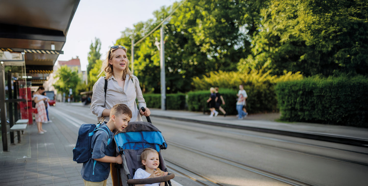 A woman is pushing a stroller with two children in it.